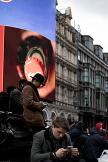 man in brown coat, men using smartphones near brown building HD wallpaper