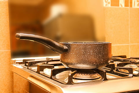Boiling water in red pot pan on top of stove flames with smokes