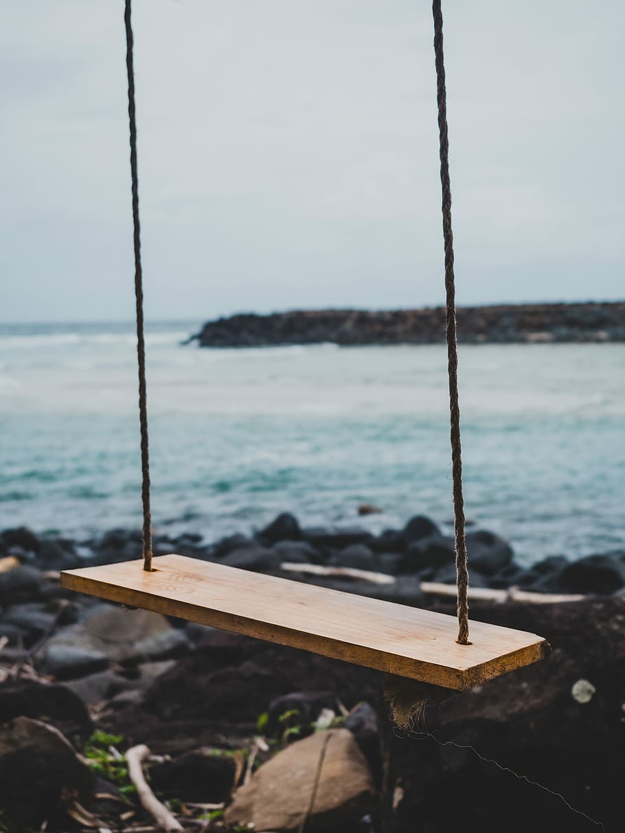 brown wooden swing chair beside shoreline, selective focus photograph of brown swing HD wallpaper