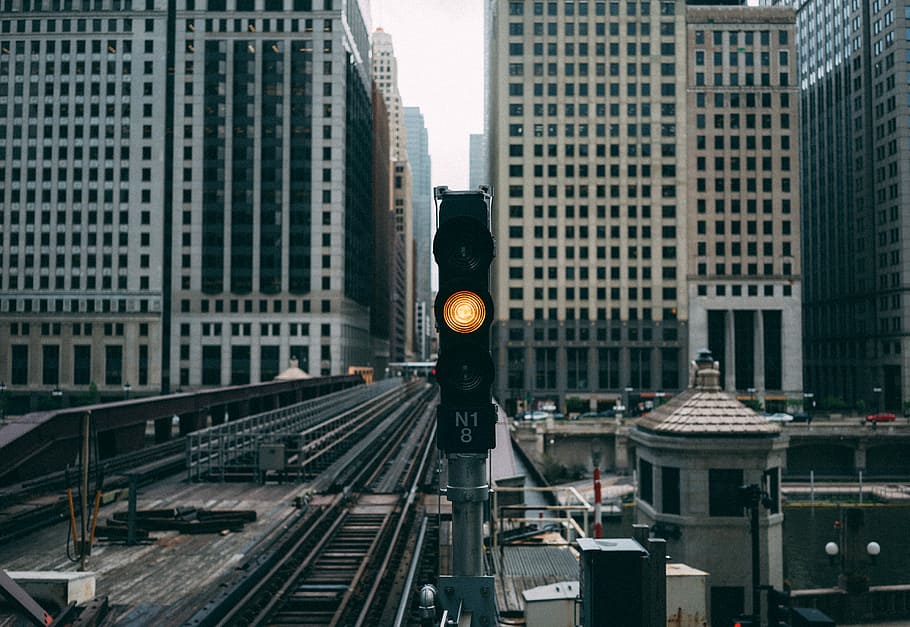 ready traffic light near railroad between buildings, black train station stoplight displays yellow light with view of high-rise buildings during daytime photo HD wallpaper