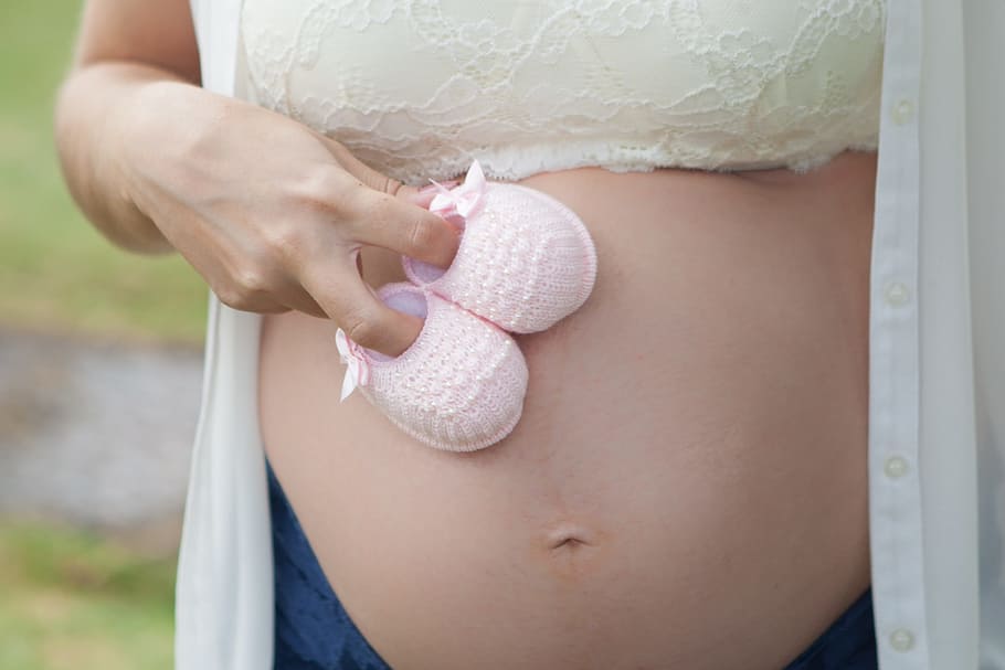 maternity photo-shot holding pink knitted shoes, pregnant woman