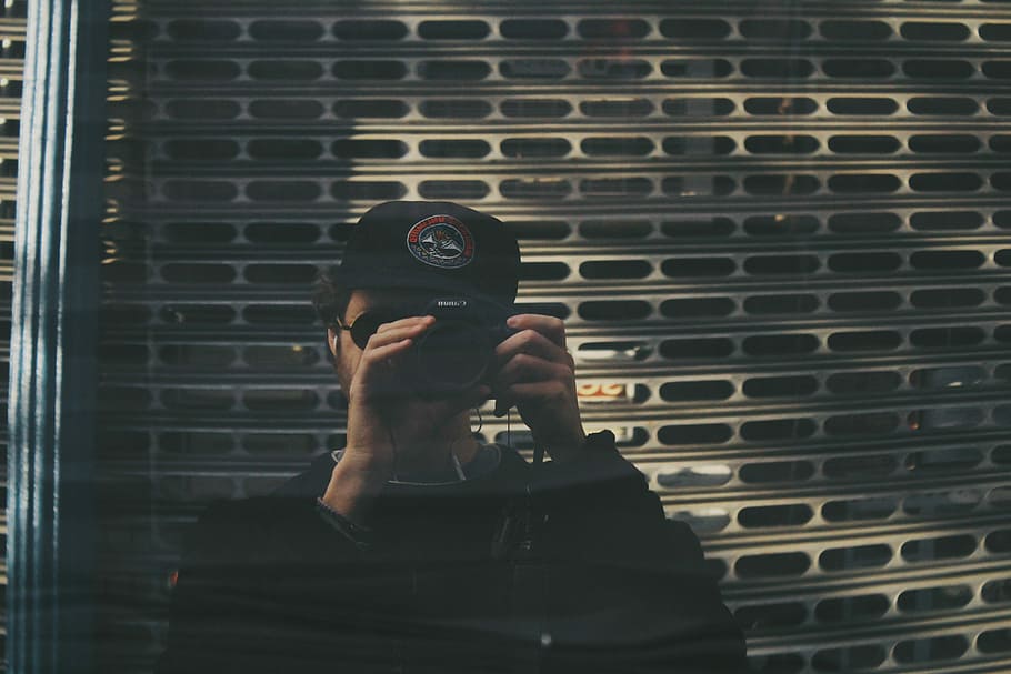 man holding camera taking photo, man taking photo near white metal wall HD wallpaper