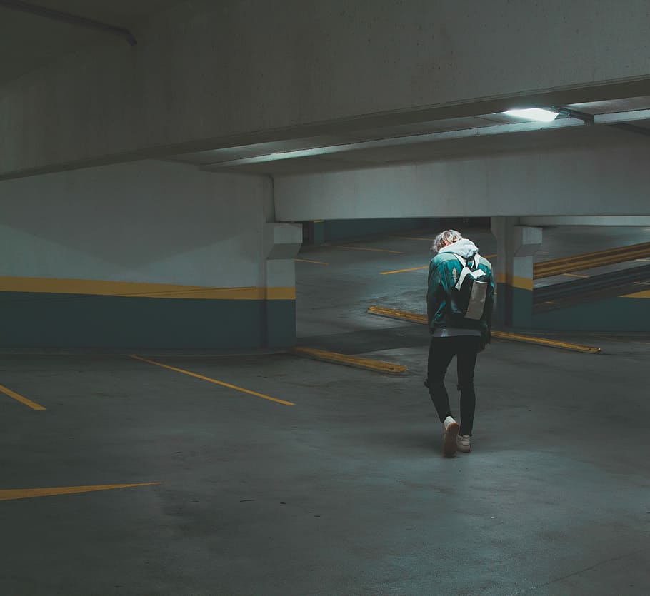 person walking on underground parking area, man in white and black backpack walking in parking lot