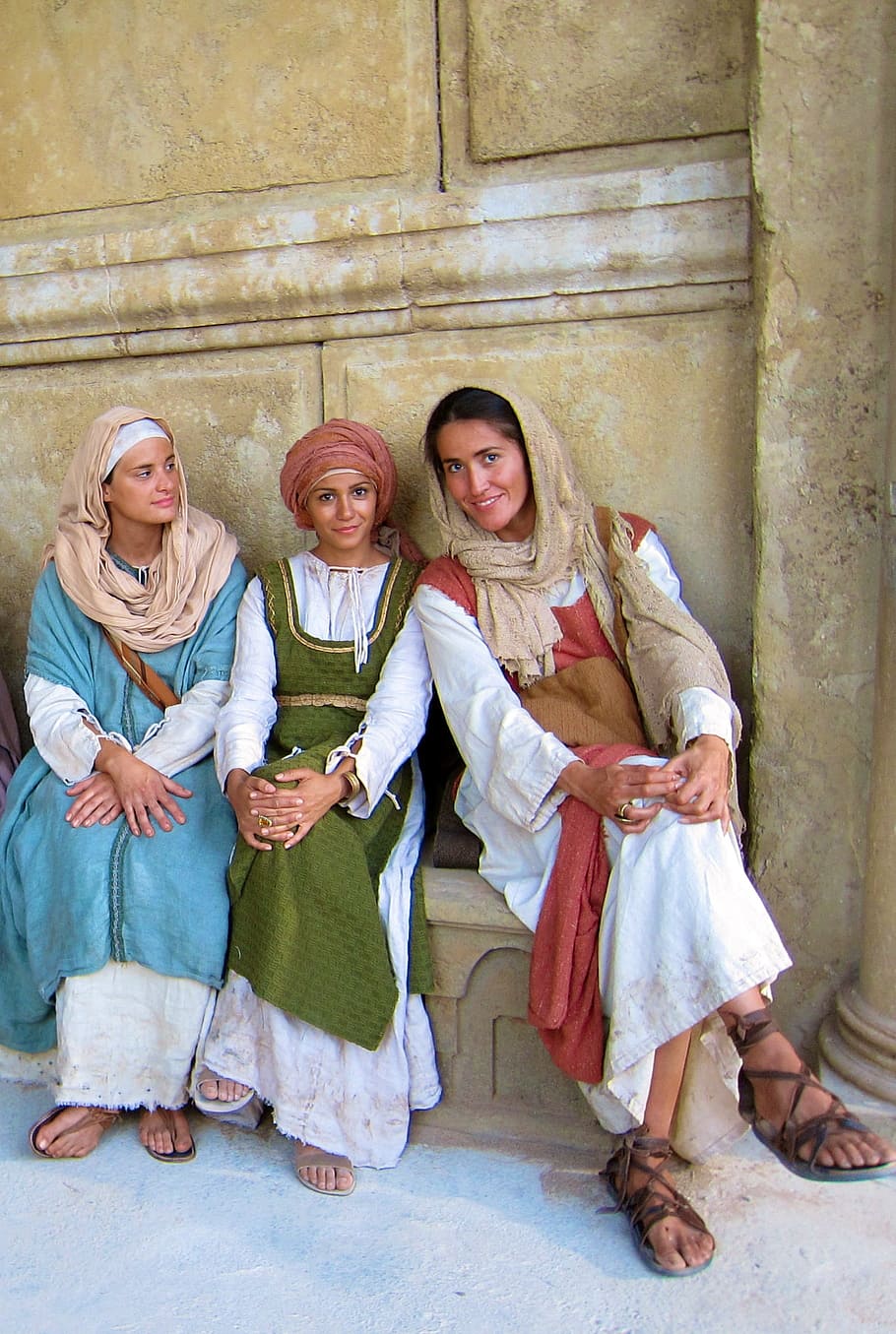women in traditional dress sitting on brown bench next to beige painted wall during daytime