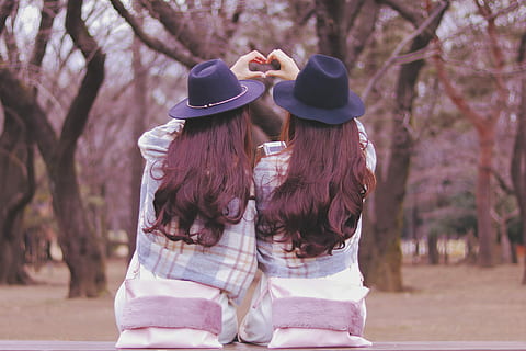 two women wearing purple hat and white and blue plaid jackets facing the trees sitting on the bench at daytime HD wallpaper