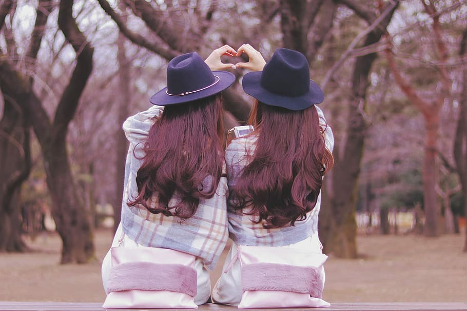 two women wearing purple hat and white and blue plaid jackets facing the trees sitting on the bench at daytime HD wallpaper