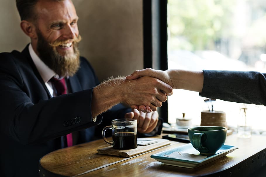 man in black suit in front of coffee on table shaking hands on person in other side HD wallpaper