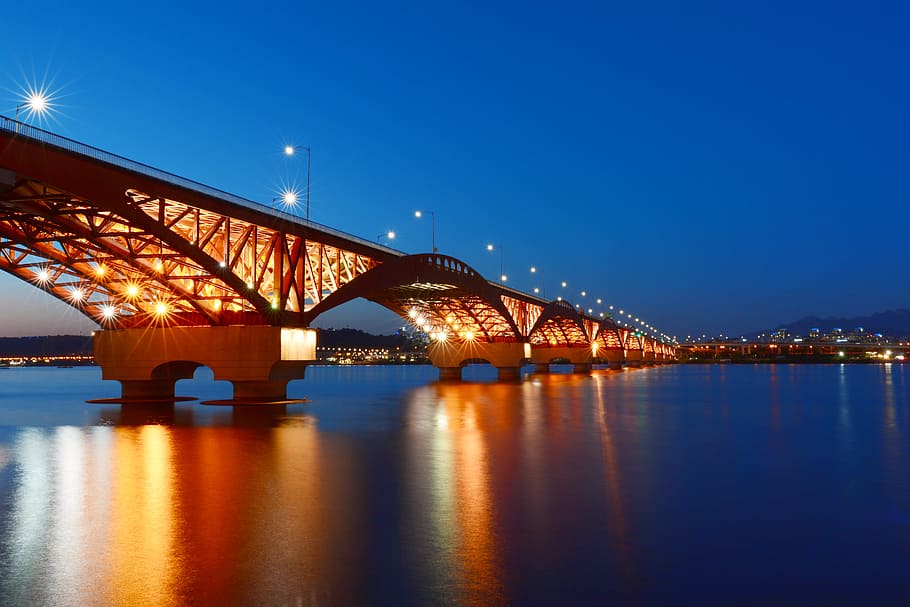 photo of calm body of water under bridge with lights at night