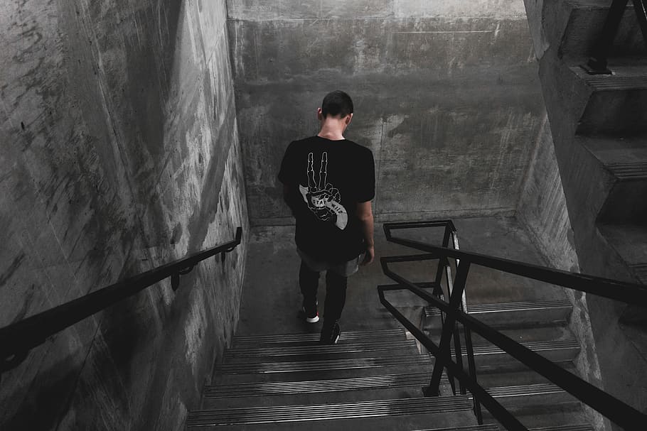man wearing black shirt walking down the stairs, man looking down standing on staircase