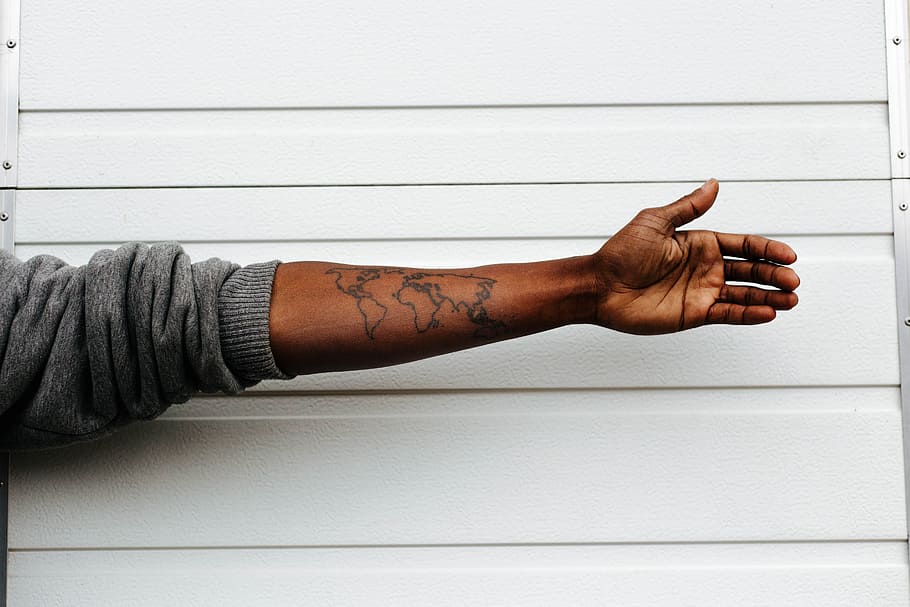 man raising hand with map arm tattoo behind white painted wall, person's hand HD wallpaper