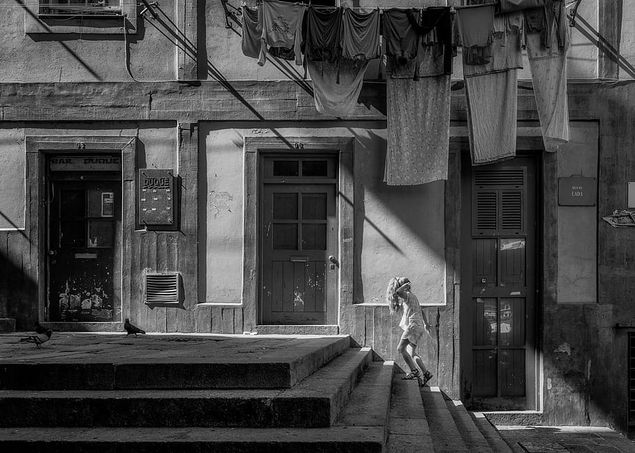 gray scale photo of girl on stairs under assorted hanged clothes