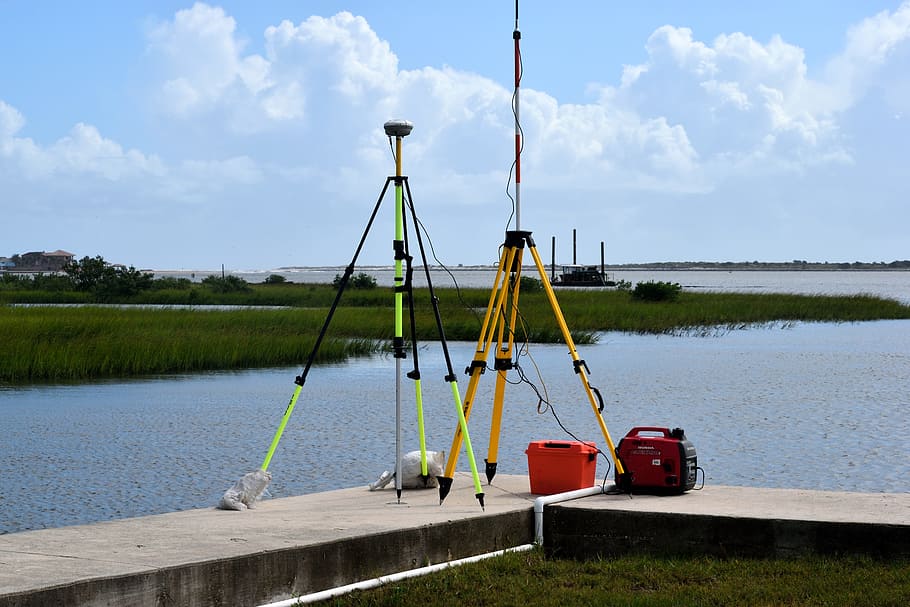 two orange, black, and green tripods beside body of water, surveying equipment