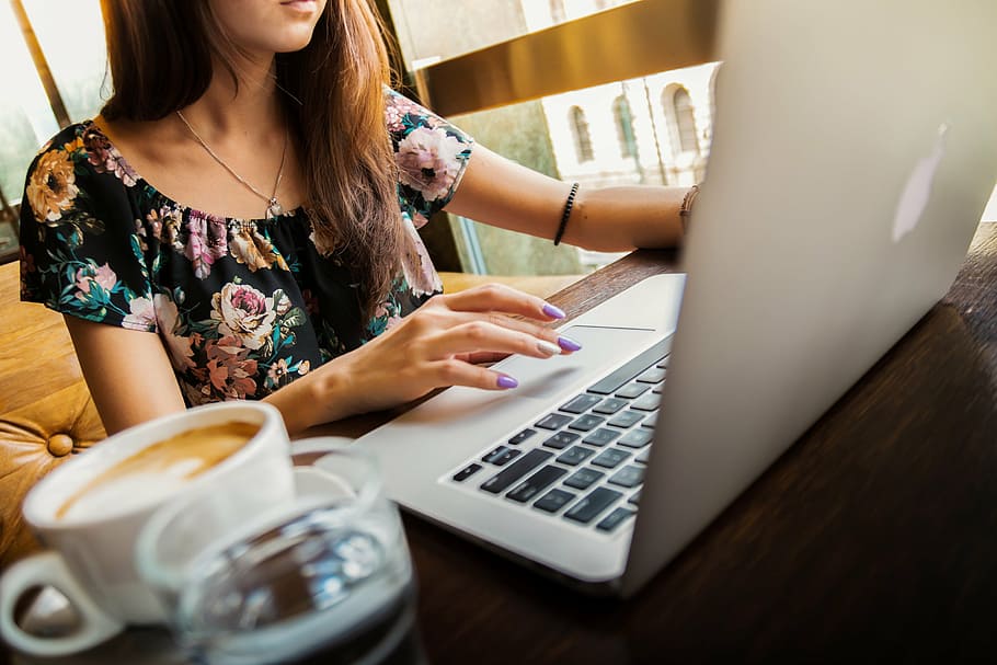 woman in black and multicolored floral shirt using MacBook while sitting HD wallpaper