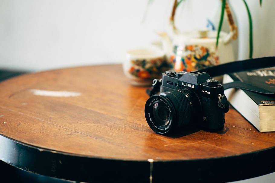 black DSLR camera on top of brown wooden table, black Fujifilm SLR camera on top of brown table
