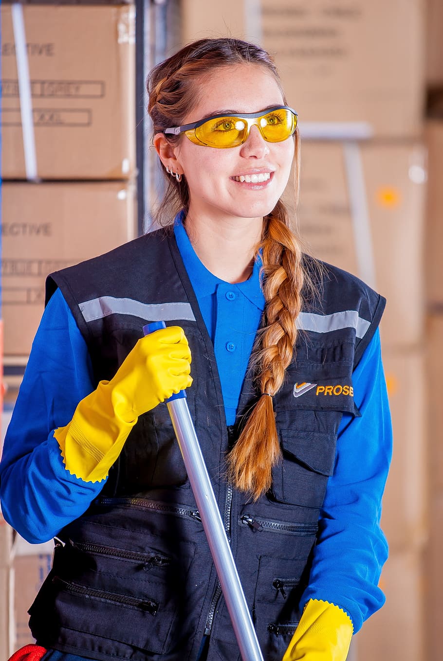 smiling woman holding gray metal rod while standing beside stacked cardboard boxes HD wallpaper