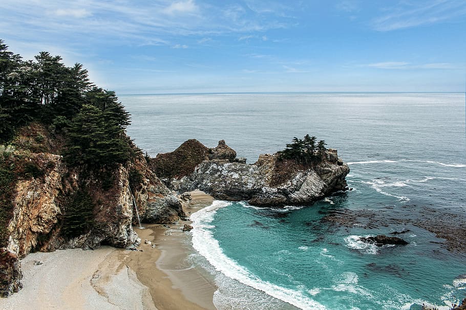 high-angle photo of green sea near white sand beach, gray and brown rocky mountain near sea under cloudy sky HD wallpaper