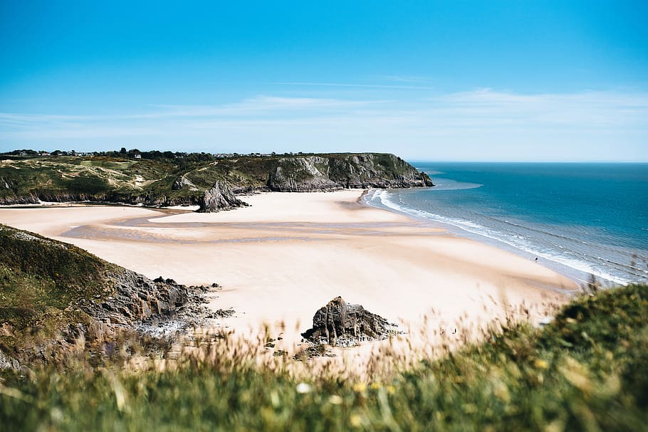 landscape photography of beach, seashore with green hills nearby at daytime HD wallpaper