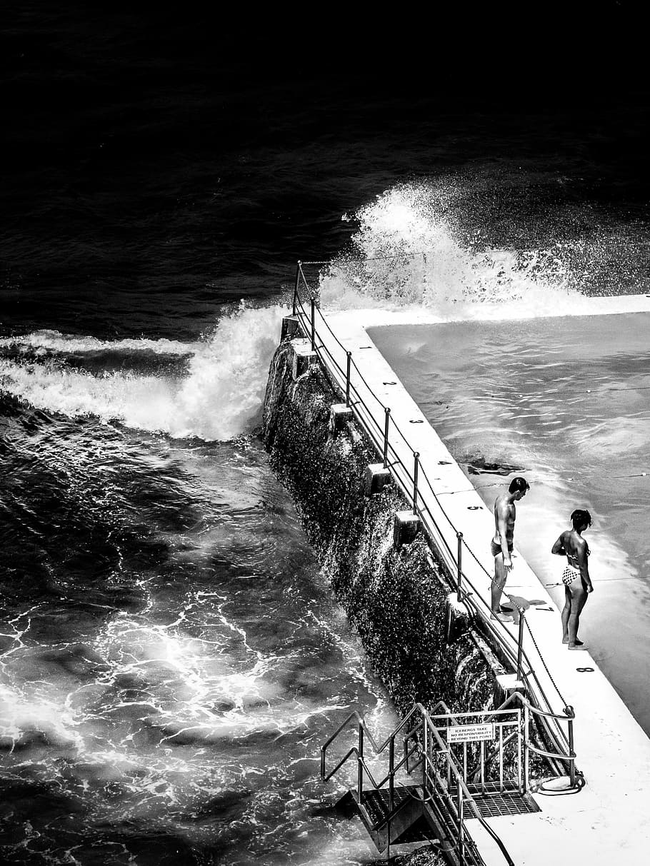 greyscale photo of two person standing on side of swimming pool near body of water HD wallpaper