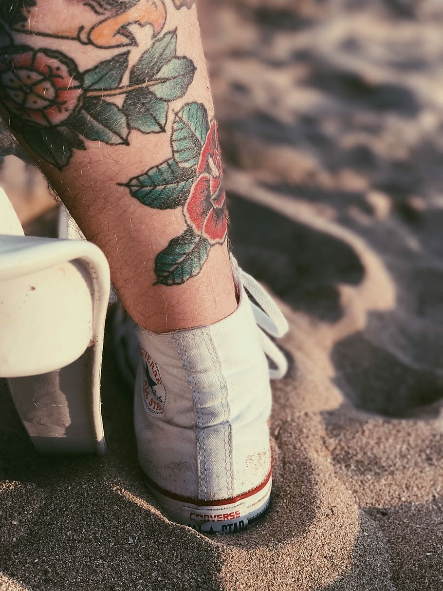 person with red rose tattoo on left leg, person standing on sand