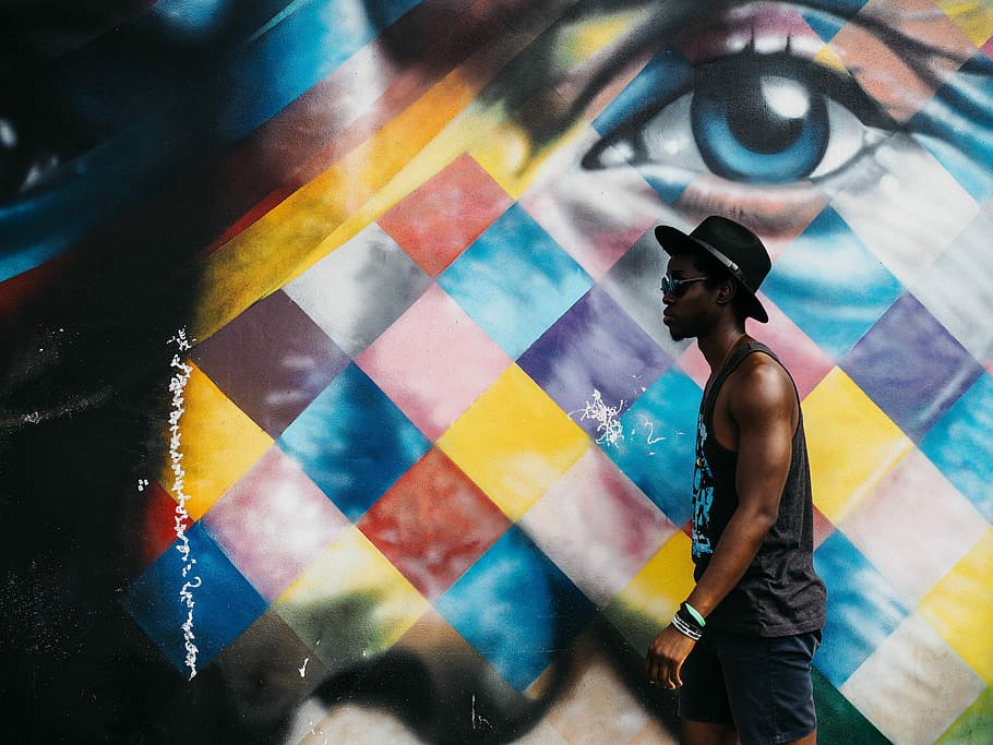 man in black tank top wearing black bucket hat beside wall art, man wearing grey tank top and black hat walking across eye wall paint HD wallpaper