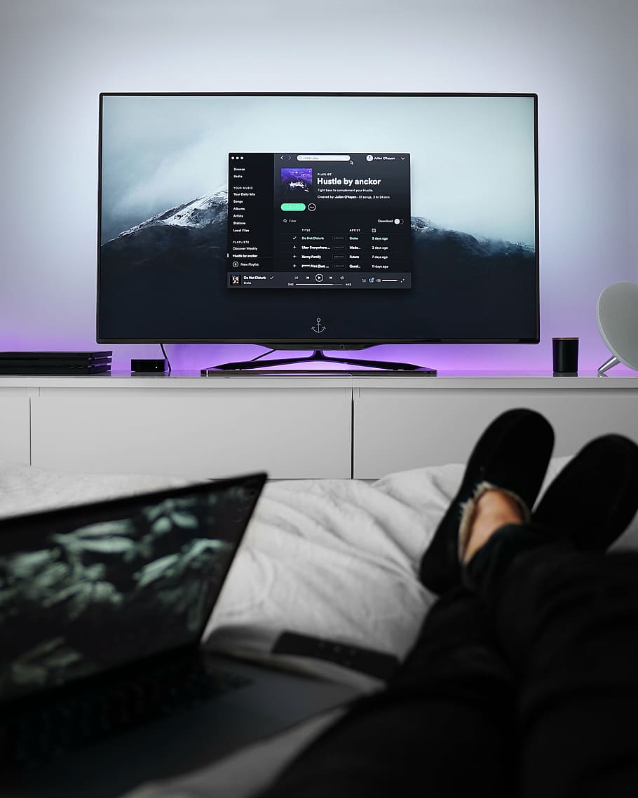 person reclining on bed near flat screen TV displaying Spotify