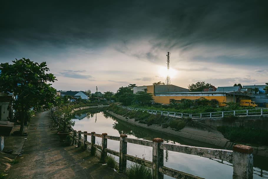 Road Beside Calm Body of Water, architecture, clouds, fence, grass HD wallpaper