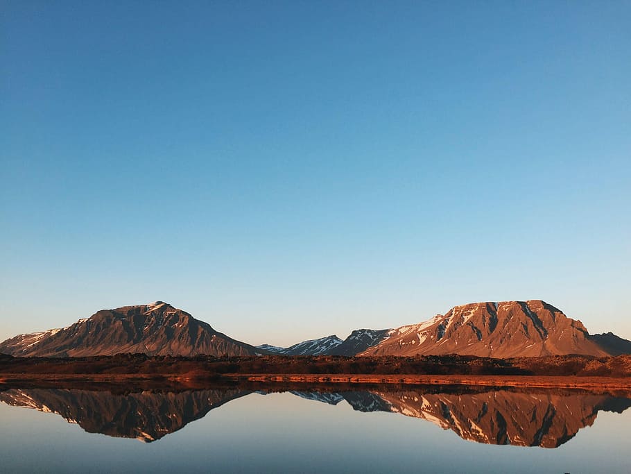 calm lake reflecting rock cliffs and clear blue skies, landscape photography of brown mountains with body of water under clear blue sky HD wallpaper