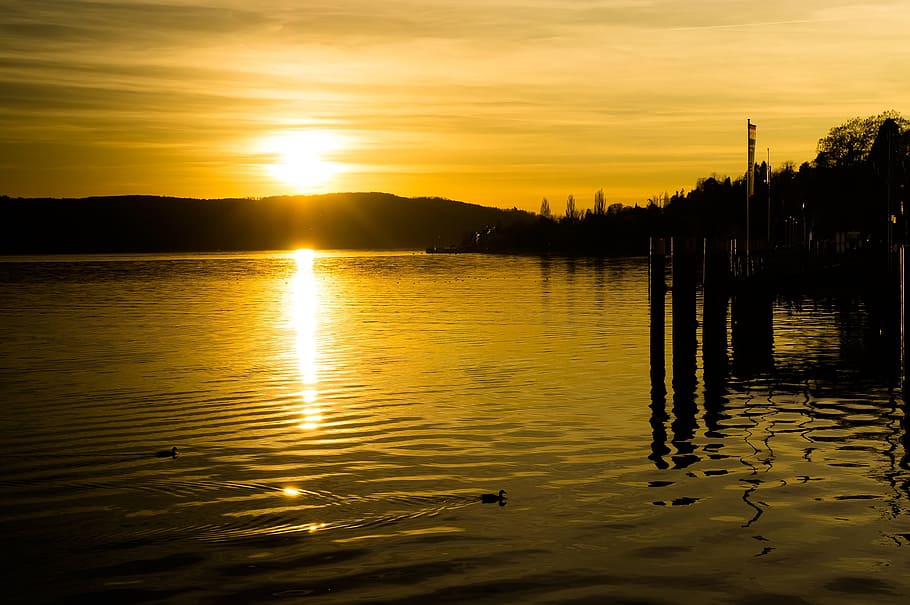 body of water across silhouette of mountain, sunset, yellow HD wallpaper