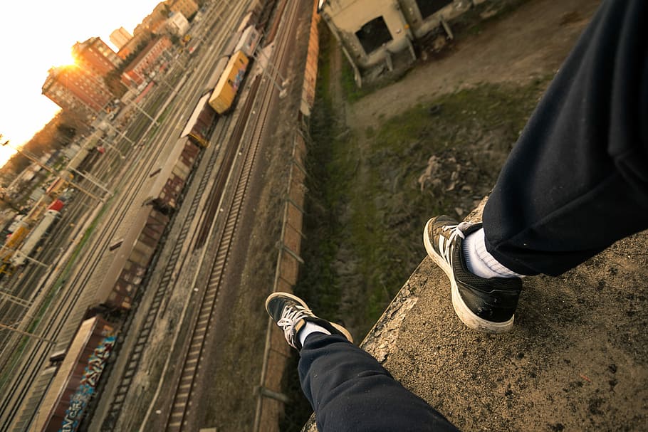 person sitting on rooftop, man sitting on gray concrete flooring near train tracks and building HD wallpaper
