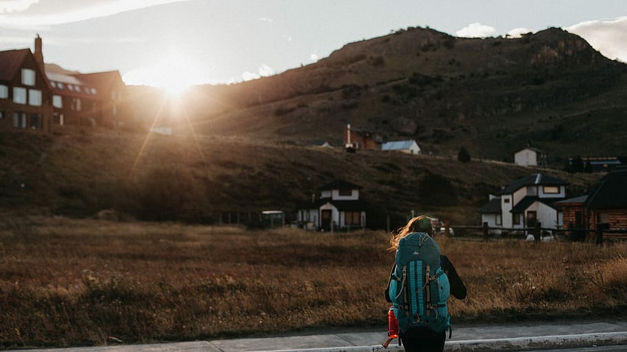 person walking on road staring at houses, woman carrying hiking backpack standing on asphalt road facing houses atduring daytime HD wallpaper