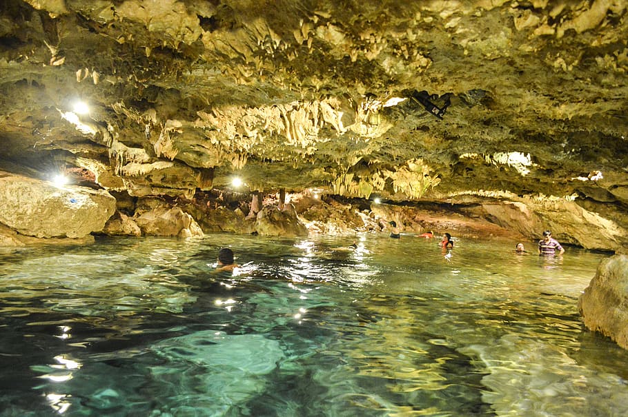 group of people swimming in body of water inside cave, cenote