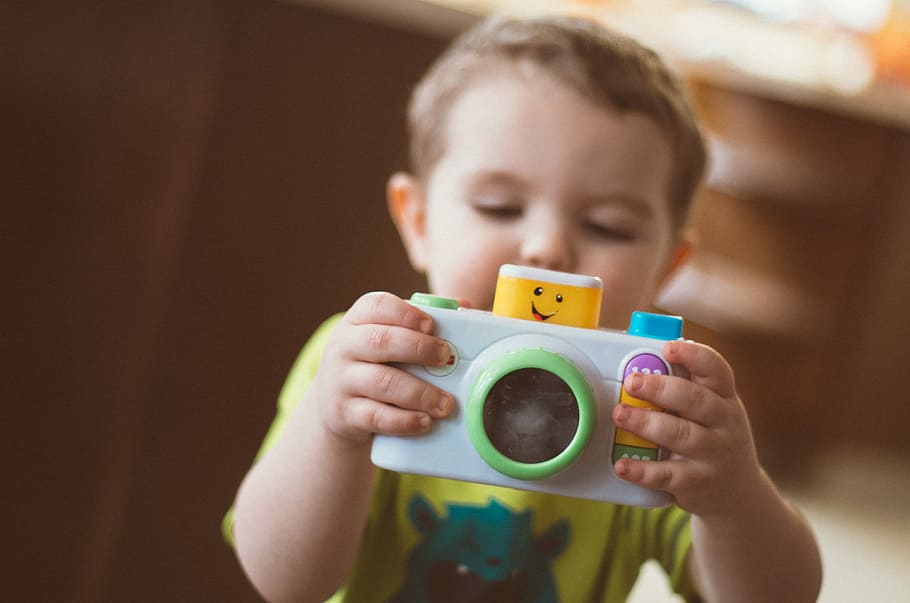 toddler holding white camera toy, toddler wearing green t-shirt holding white and green plastic camera toy while playing, HD wallpaper