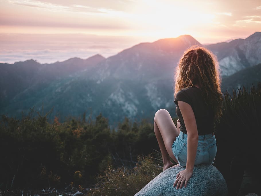 woman sitting on rock, woman sitting on gray stone in front of white and black mountain at golden hour HD wallpaper