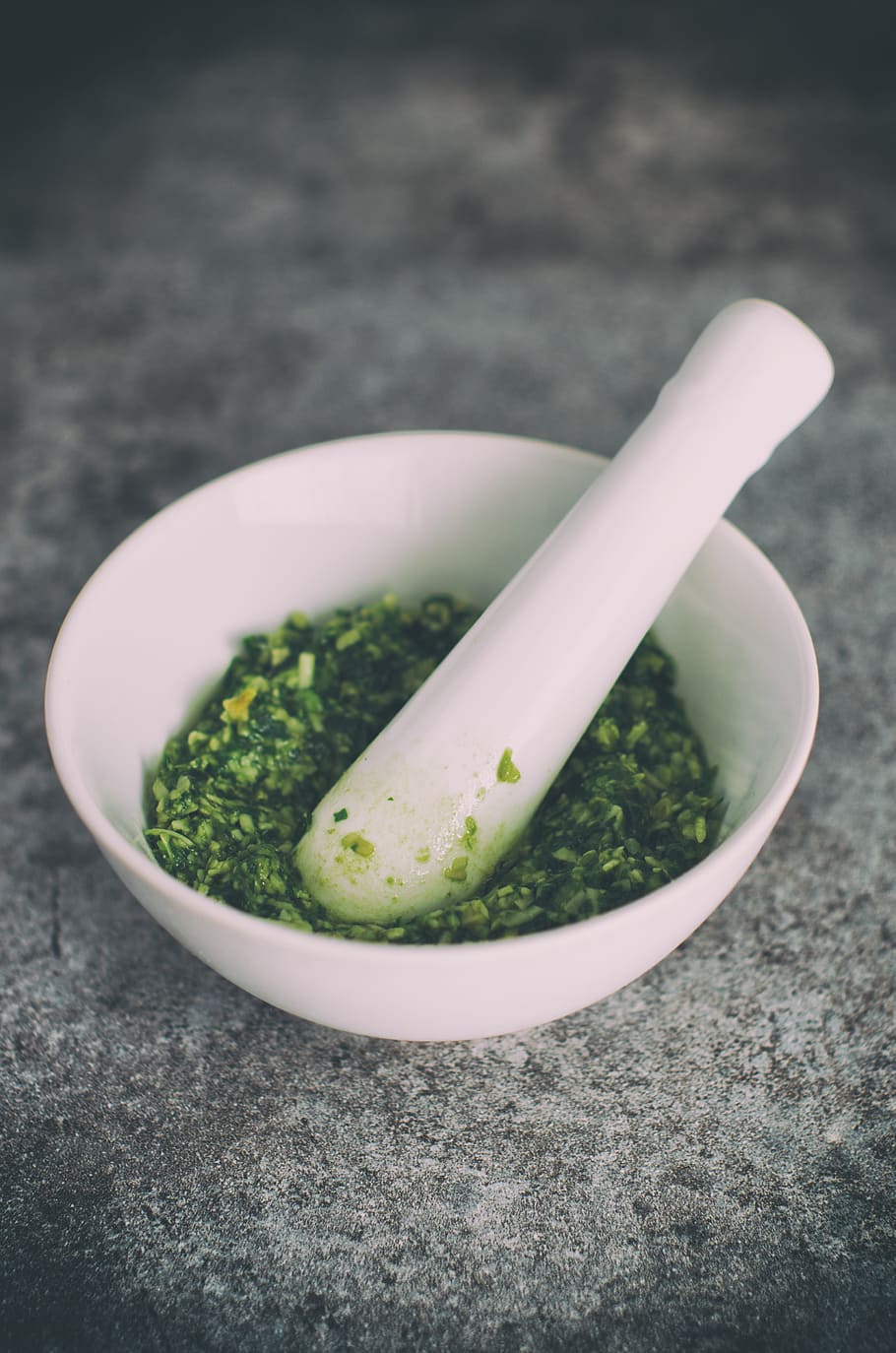 vegetable grind in mortar and pestle, white ceramic bowl with pestle and green leaf spices