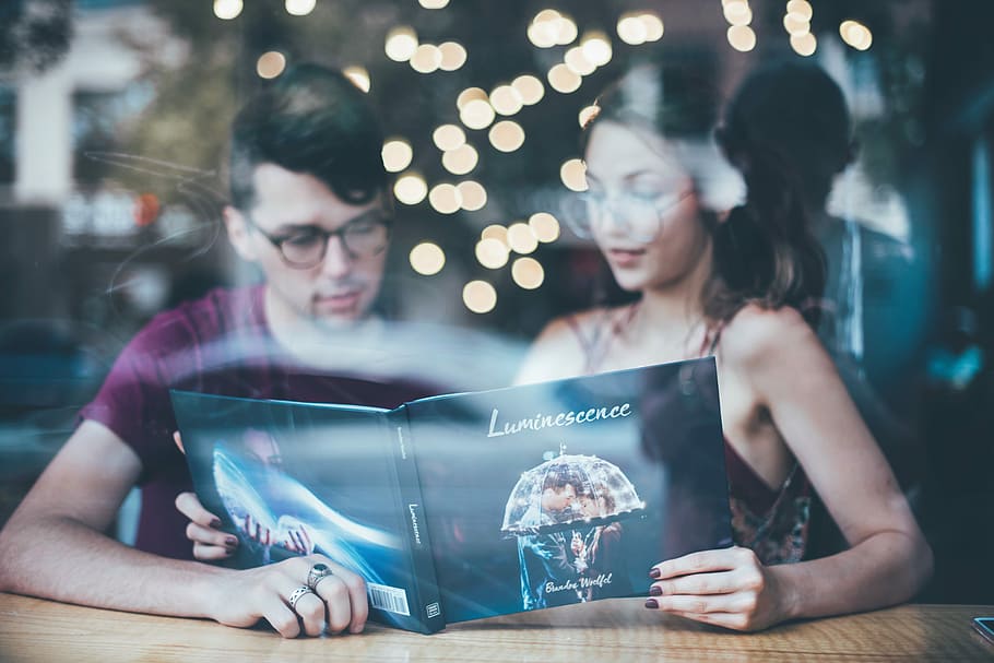 man sitting beside woman while reading, man and woman reading Luminescence book with bokeh lights on background HD wallpaper