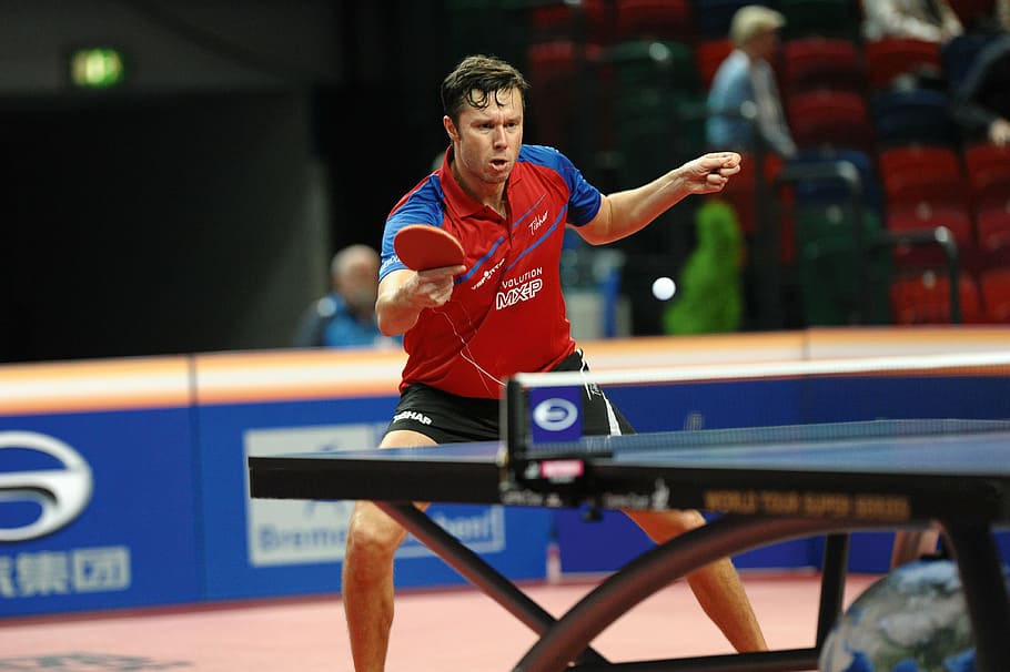 man in red and blue polo shirt playing table tennis, ping pong