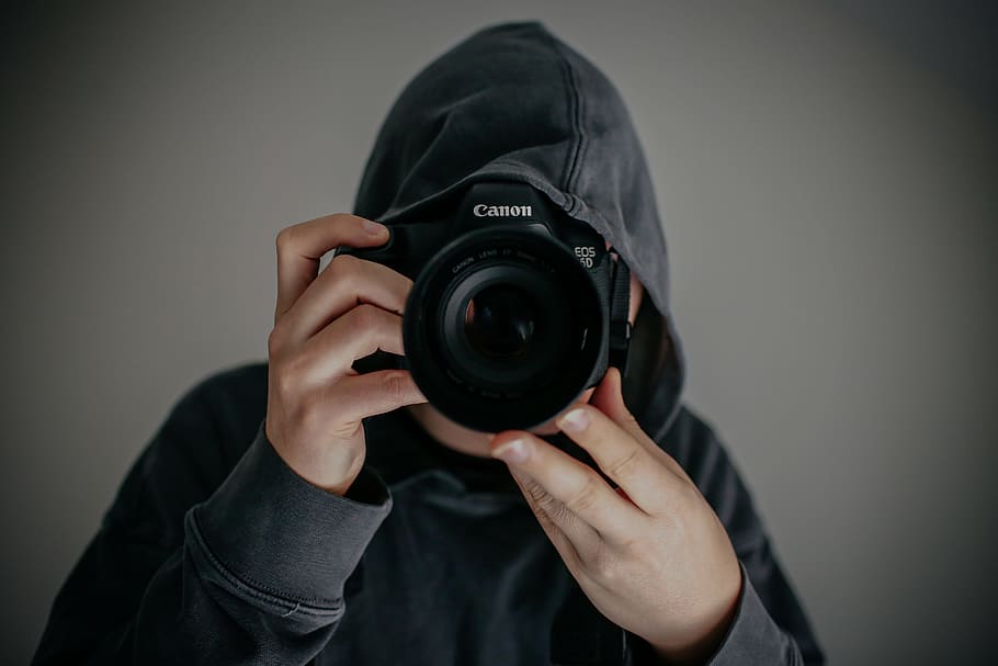 person holding Canon camera, person wearing gray hoodie holding Canon DSLR camera