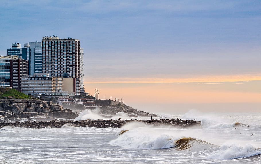 sea wave splashing in seashore, curtain wall building near sea at daytime HD wallpaper