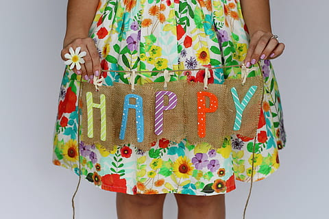 person wearing yellow and red floral dress holding happy text printed hanging decor HD wallpaper