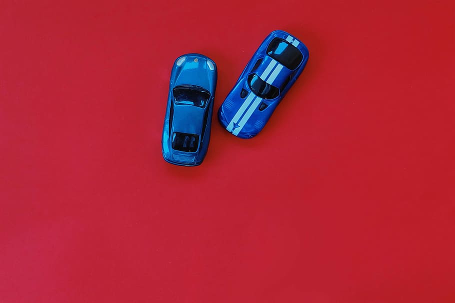 two blue die cast toy cars on red wooden table top, matchbox