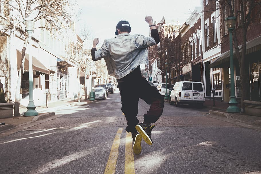 man jumping on the middle of the street during daytime, man wearing white jacket and black pants about to jump on street during daytime HD wallpaper