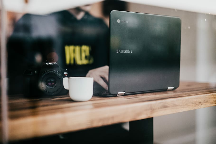 person using black Samsung laptop with cup and camera, person in front of laptop beside DSLR camera on table, HD wallpaper