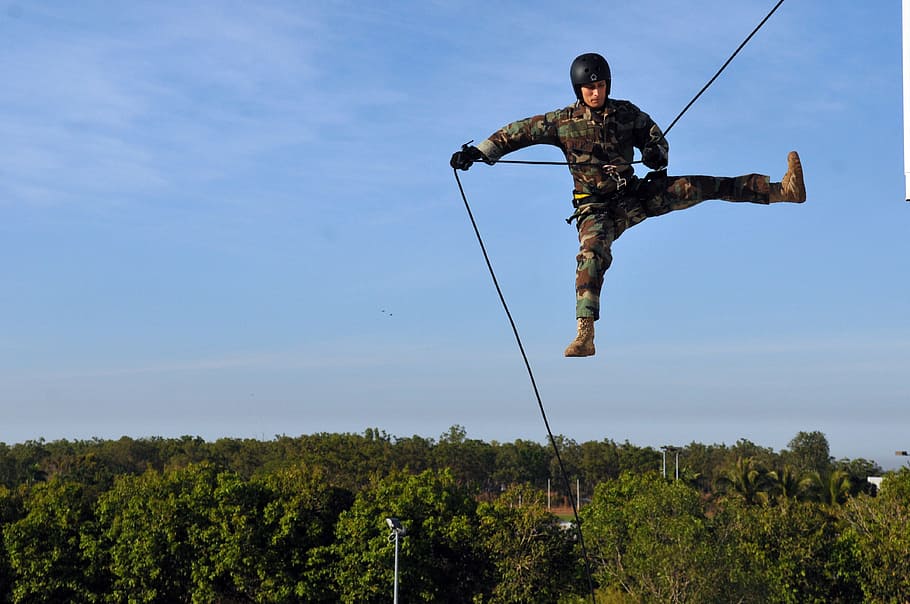 soldier in mid-air wearing camouflage suit holding on rope below green leafed trees during daytime, HD wallpaper