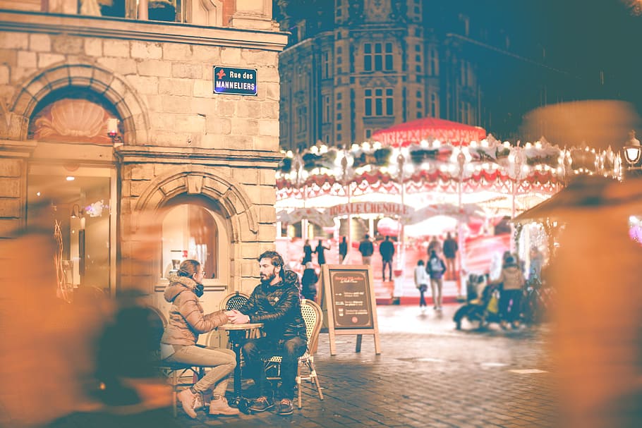 couple sitting beside building near carousel during night time, man and woman sitting on two chairs HD wallpaper