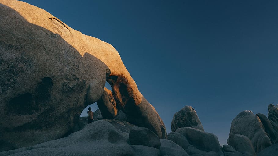 brown natural arch under clear sky, person standing on rock formation under clear sky HD wallpaper