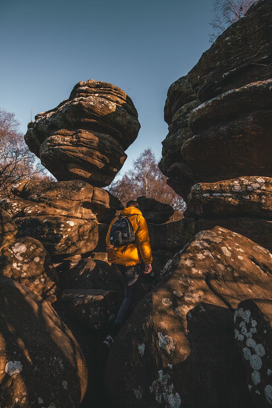 person wearing jacket carrying backpack, person standing under boulder HD wallpaper