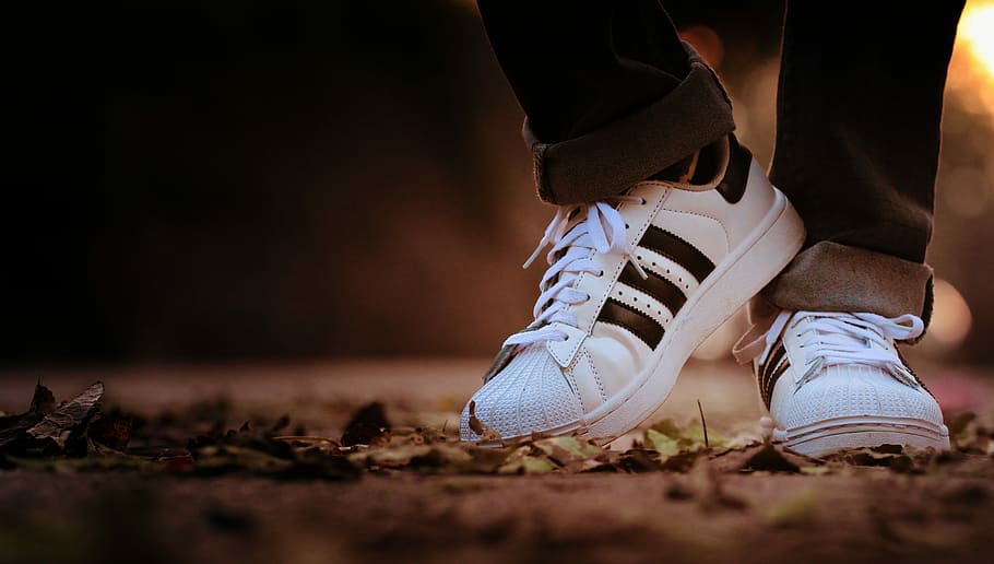 shoes, person in black jeans wearing pair of white-and-black adidas sneakers