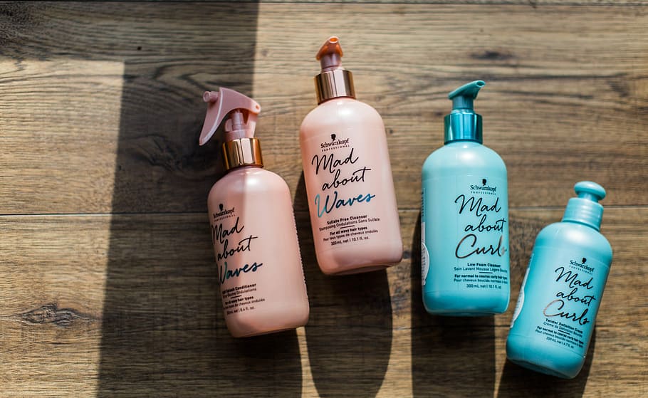 four Mad About Curl and Waves labeled bottles on wooden surface, four pink and teal pump bottles HD wallpaper