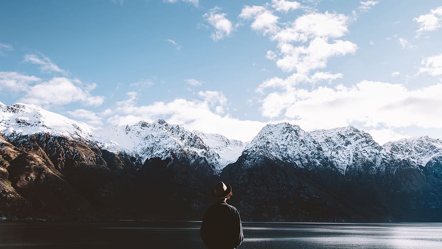 person wearing hat looking at snow covered mountain under blue sky, person facing mountain covered with snow under cloudy sky HD wallpaper