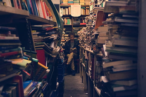 man sitting reading book on the end of pile of book racks, man sitting in library HD wallpaper